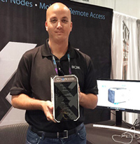 A man in a black polo shirt holds up a rectangular piece of electronic hardware.