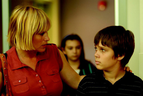 A blonde woman in a red shirt looks intently at a young boy with dark hair.