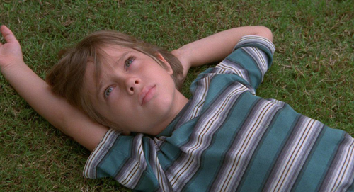 A young person in a striped shirt lies on green grass with arms stretched above their head.