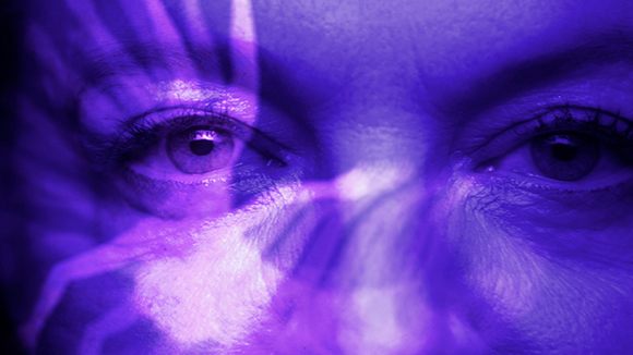 Close-up of a person's eyes illuminated by purple light and abstract light patterns.