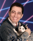 A smiling man in a grey sweater holds a black and white kitten against a dark background with blue and pink light streaks.