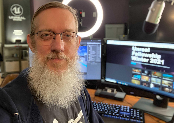 A man with glasses and a long grey beard looking forward in an office setting.