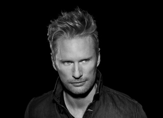 Black and white portrait of a man with styled hair looking slightly to the side against a dark background.