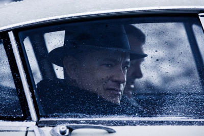 A man wearing a dark fedora looks out through a frost-covered car window.
