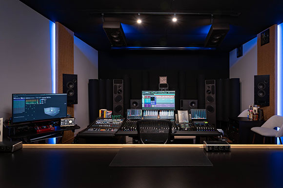 A professional recording studio featuring a large mixing console, multiple computer monitors, and studio speakers.
