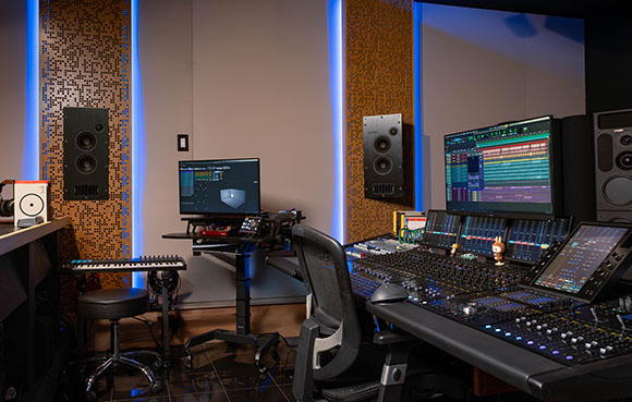 A music studio featuring studio monitors, computer screens, and a large mixing console.