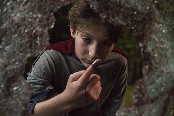 A young boy with brown hair looks down at a dark stain on his finger through a circular, textured frame.