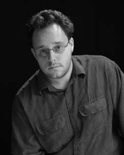 Black and white portrait of a man with curly hair and glasses wearing a button-down shirt.