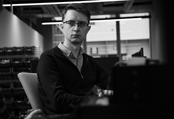Black and white portrait of a man with glasses sitting at a desk in an office.