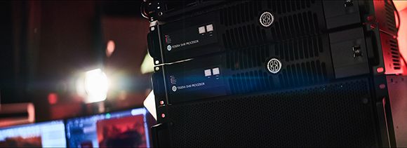 Stack of black rack-mounted audio processors with glowing logos in a dimly lit studio setting.