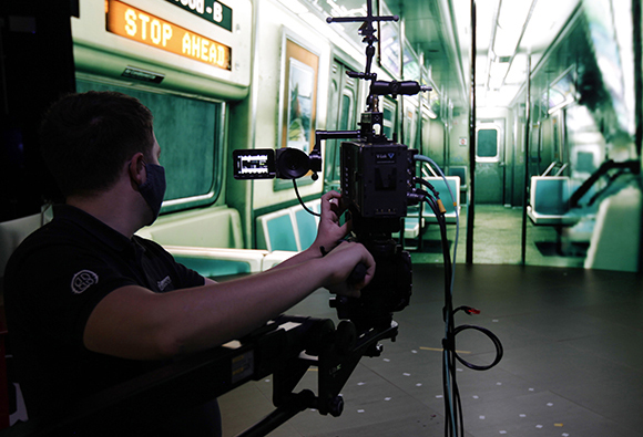 A person uses a professional camera on a dolly inside a subway car.