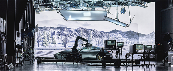A dark car sits in a studio before a massive LED screen displaying a snowy mountain landscape.