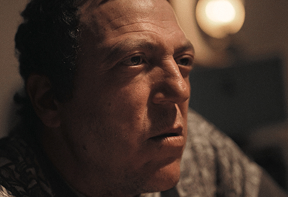 Close-up of a man with dark hair looking to the side in warm, dim lighting.