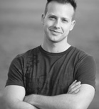 A smiling man with short hair wearing a dark t-shirt and crossing his arms.