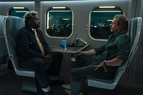 Two men sit in high-backed seats facing each other in a train car at night.