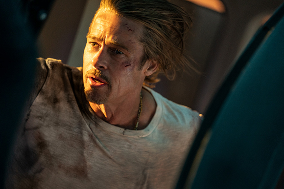 A man with messy blonde hair and a stained white t-shirt looks off-camera with a serious expression.