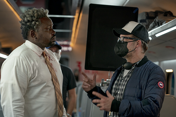A man in a white shirt with blood stains talks to a man in a blue jacket and baseball cap.