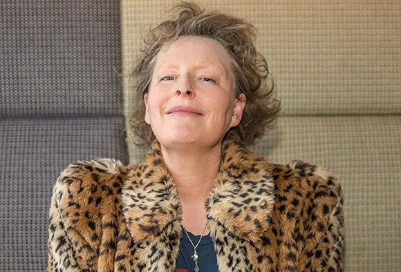 A woman with curly hair wearing a leopard print faux fur coat and smiling at the camera.