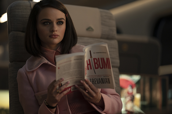A woman with dark hair wearing a pink coat sits in a chair reading a magazine titled Hibumi.