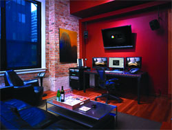 A media room featuring a red wall, a large TV, a computer desk with monitors, and a brick wall with a window.