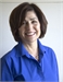 A smiling woman with short brown hair wearing a bright blue button-down shirt against a white background.
