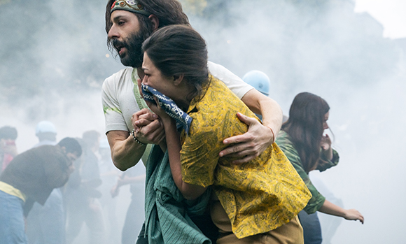A man in a headband embraces a woman in a yellow patterned shirt amidst thick white smoke.