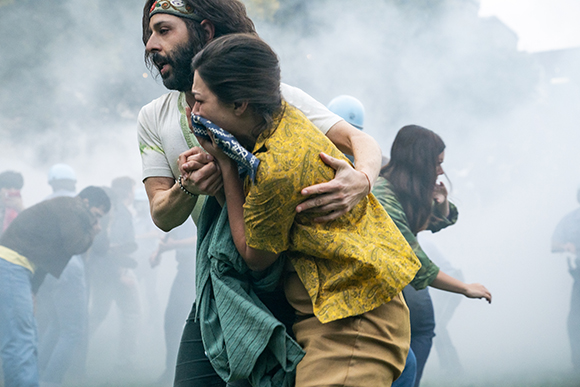A man in a headband carries a woman in a yellow patterned shirt through thick white smoke.