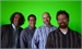 Four men smiling and posing together against a solid green backdrop.