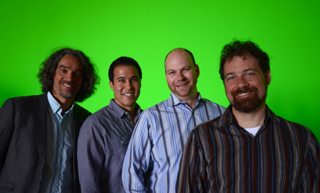 Four men smiling and standing side-by-side against a solid green backdrop.