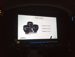 A large projection screen in a dark theater displays a slide titled 'PRIME LENSES' with images of three camera lenses.