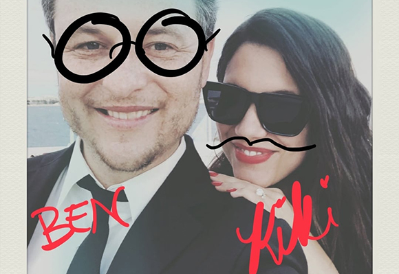 A man in a suit and a woman in sunglasses with digital glasses and mustache stickers and names written in red.