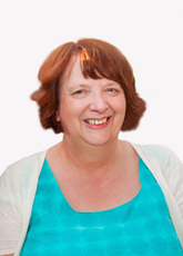 A smiling woman with reddish-brown hair wearing a turquoise top and a white cardigan.