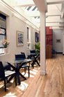 A bright room with wooden floors, white walls, small tables, and black chairs under a skylight.