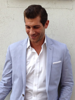 A smiling man wearing a light blue blazer over a white button-down shirt.