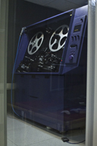 A large blue vintage film projector with two large reels inside a glass display case.