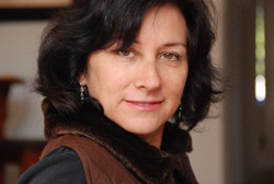 A woman with dark, wavy hair and brown eyes smiles slightly toward the camera.