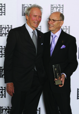 Two men in suits stand together, one holding an award.