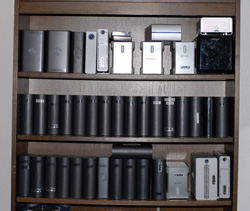 Three wooden shelves holding rows of silver and black electronic hardware and rectangular modules.