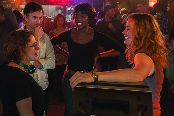 A group of diverse friends laughing and talking together in a dimly lit, crowded bar.