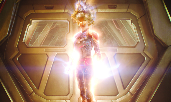 A person enveloped in bright white light stands in front of a large, geometric metal door.