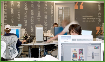 People working at desks in an office with large text on the background wall.