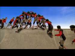 People in red and black athletic clothing performing synchronized movements on a concrete ramp under a blue sky.