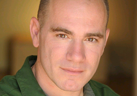 Close-up portrait of a man with short hair and brown eyes wearing a green collared shirt.