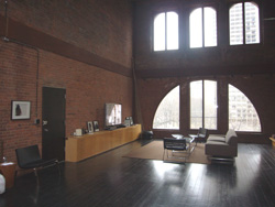 A large loft living room with red brick walls, dark wood floors, and large arched windows.