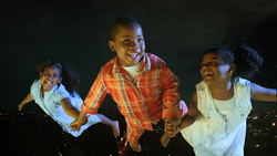 Three smiling children jumping joyfully against a dark, starry night background.