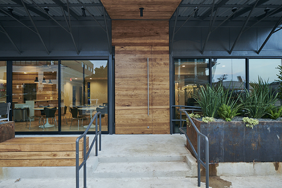 A modern building entrance featuring a large wood-paneled wall, glass doors, and concrete steps with metal railings.
