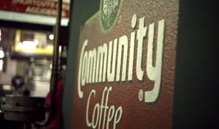 A close-up, angled shot of a red and white Community Coffee logo on a dark surface.