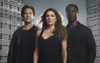 A woman in a black dress stands between two men in dark clothing against a city backdrop.