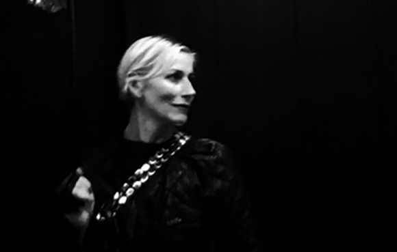 A woman with light hair wearing a dark top with a patterned strap looks to the side.