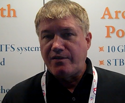 A man with short blonde hair wearing a black collared shirt and a white lanyard.